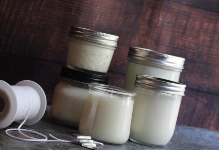 Mason jars filled with white candles and a spool of wicking.