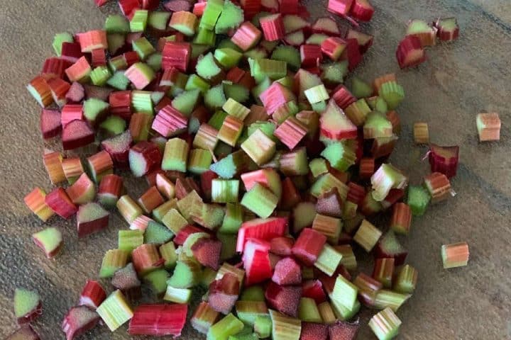 Chopped rhubarb pieces scattered on a textured surface, showing varying shades of red and green.