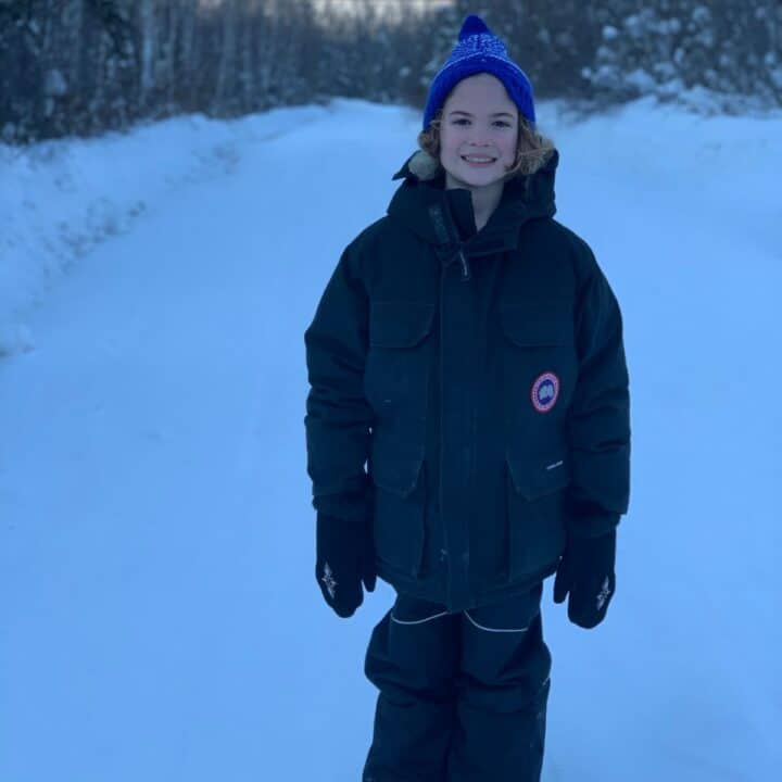 Child dressed in warm winter gear for foraging with snow and trees in background