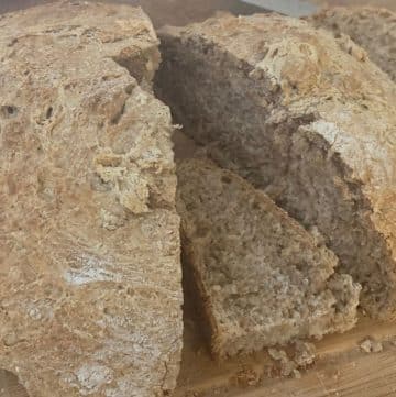 A loaf of whole grain bread is partially sliced, resting on a wooden cutting board.