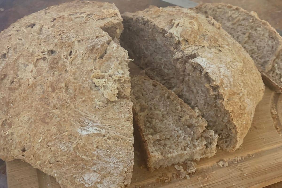 A loaf of whole grain bread is partially sliced, resting on a wooden cutting board.