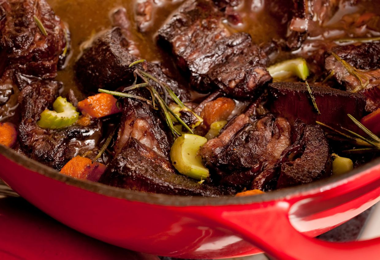Beef stew in a red pot on a table.
