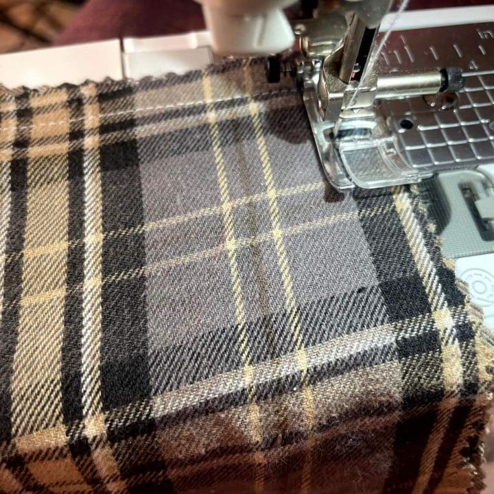 A sewing machine is sewing a plaid fabric.