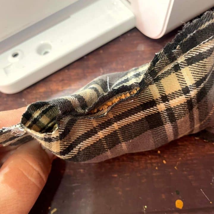 A hand holding a piece of plaid fabric on a table.