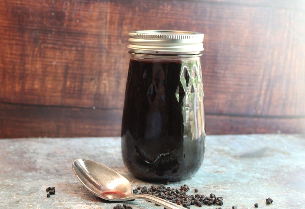A jar of black pepper syrup next to a spoon.