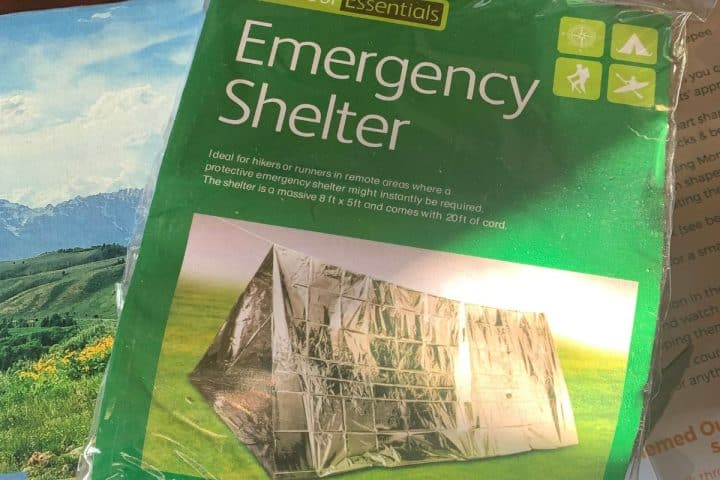 Packaging of an Emergency Shelter, designed for hikers and runners in remote areas as part of survival preparedness for beginners, 8 ft x 5 ft with 20 ft of cord. The package is labeled "Essentials" with illustrations for various outdoor activities.