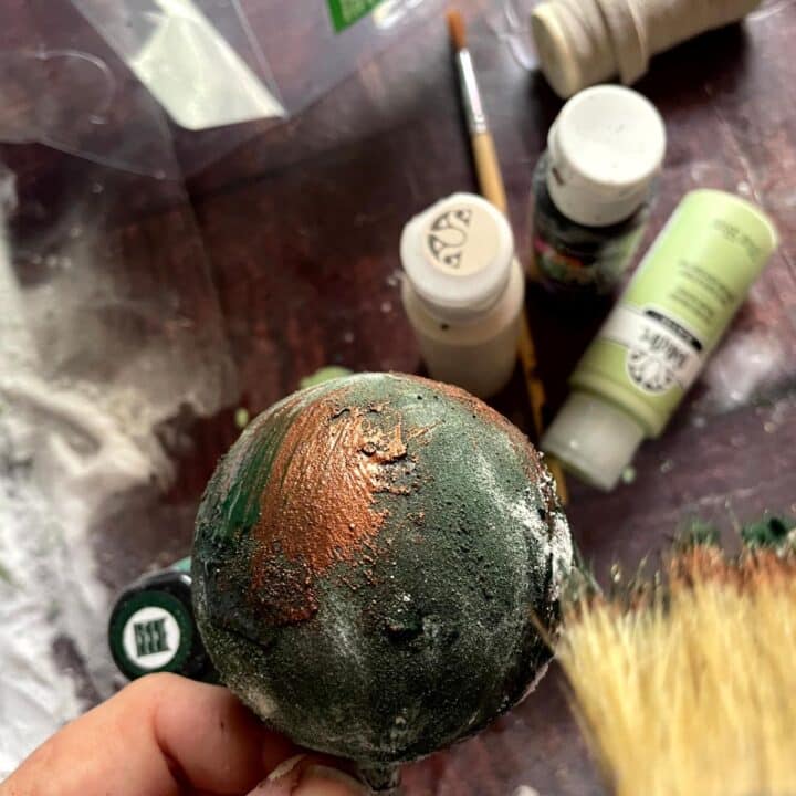 A person is painting a green ball with paint and brushes.