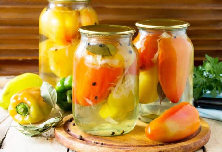 Three jars of pickled peppers on a wooden table.