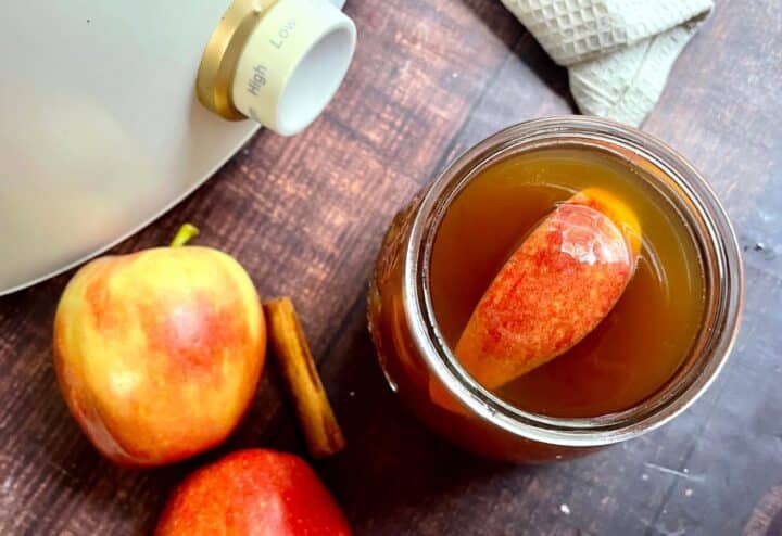 A jar with apples and cinnamon next to it.