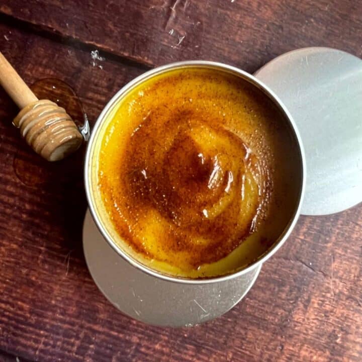 Honey beeswax coconut oil lip balm in a tin with a wooden spoon.