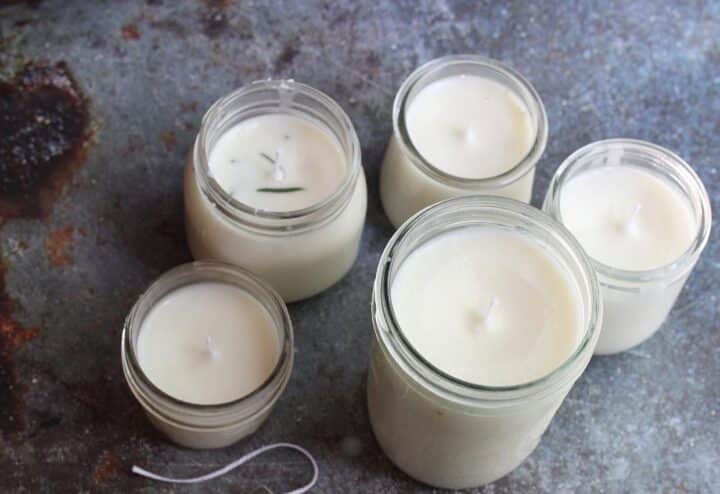 Five jars of white candles on a table.