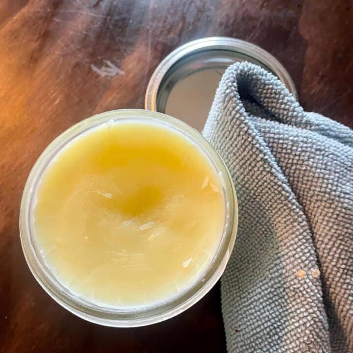 A jar of homemade beeswax furniture polish sitting on a wooden table.