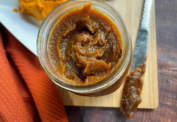 Pumpkin butter in a jar on a cutting board.