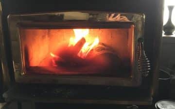 A lit wood-burning stove with visible flames and a glass door in a dimly lit room.