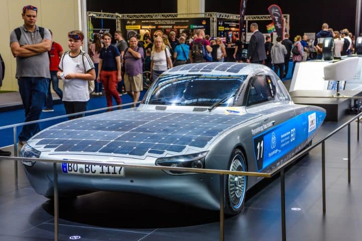 A sleek solar-powered car displayed at an exhibition, surrounded by people.