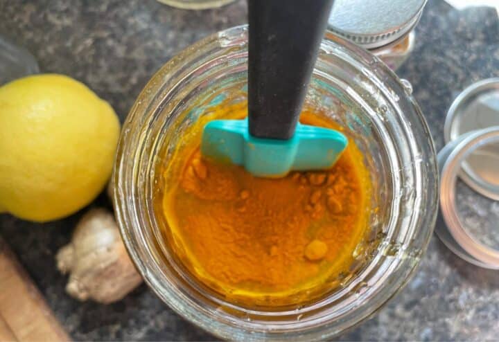 A jar of tumeric and lemons on a cutting board.