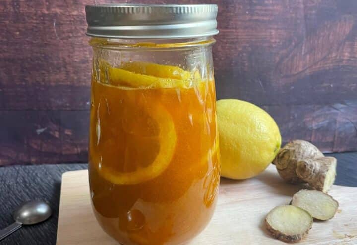 A jar with lemons and ginger on a cutting board.