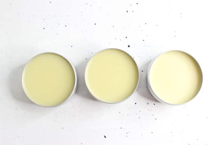 Three open tins of light yellow balm aligned horizontally on a white speckled surface.