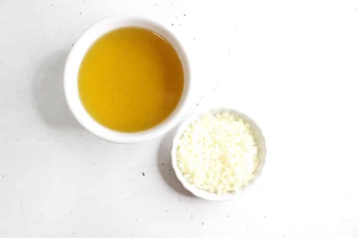 Two white bowls on a white surface; one contains a yellow liquid, and the other holds small white pellets.