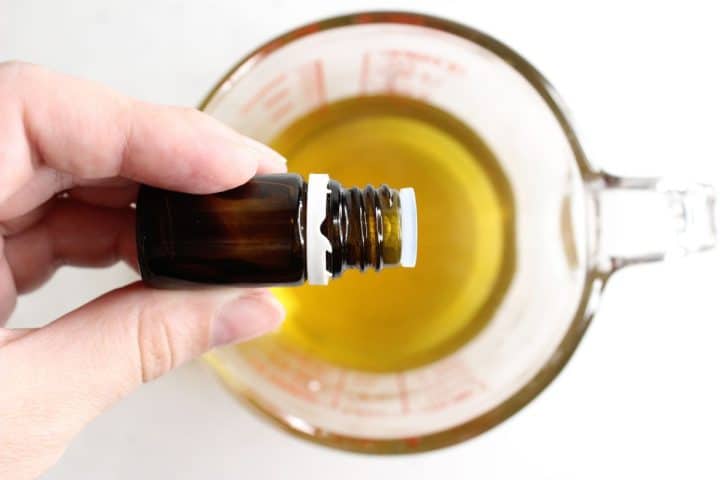 Hand holding a small brown bottle over a clear measuring cup filled with yellow liquid.