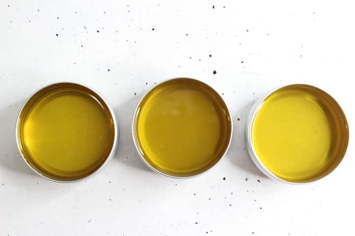 Three shallow tins filled with yellow liquid are arranged in a row on a white surface with black speckles.