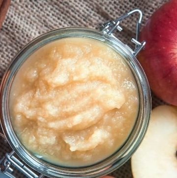 Homemade applesauce in a mason jar on a wooden tabletop with a sliced apple and cinnamon sticks