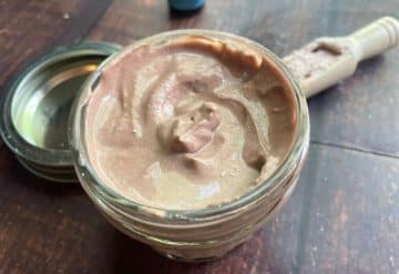 A jar of homemade calamine lotion open on a wooden table, with a spoon resting beside it.