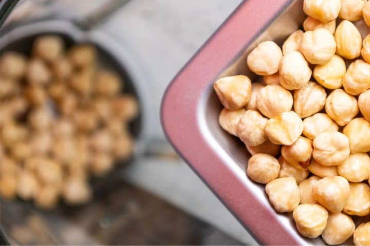 Close-up of raw hazelnuts in a metal container, with a blurred reflection in the background.