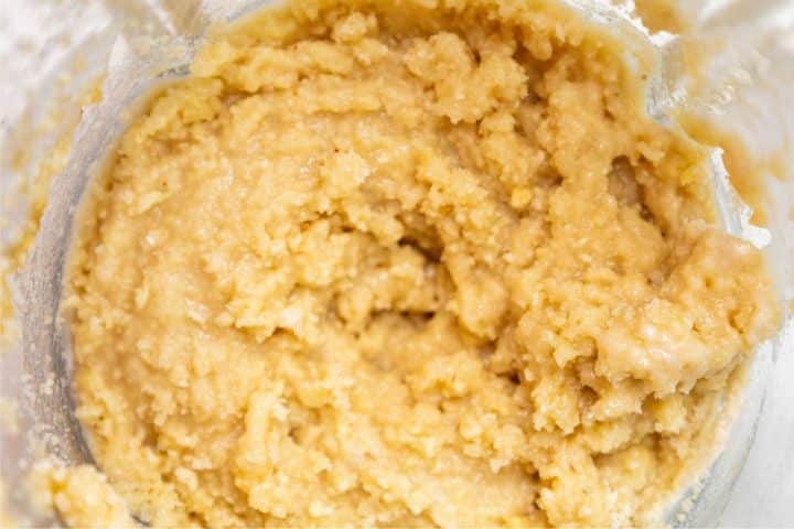 A close-up of a thick, creamy beige mixture, possibly a dough or batter, with a slightly uneven texture in a glass mixing bowl.
