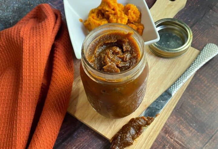 A jar of pumpkin butter on a cutting board.