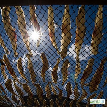 a picture of dozens of dried fish on a grate with a blue sky background