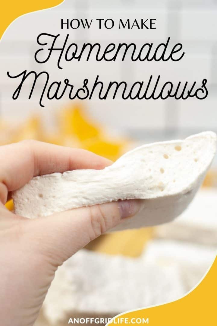 a pinterest image of a hand holding a square of marshmallow, text overlay "how to make homemade marshmallows"