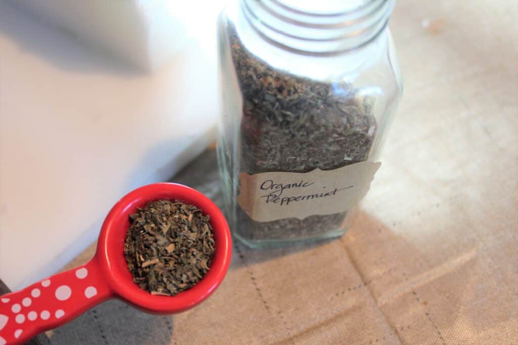 dried peppermint leaves in glass jar and red measuring spoon