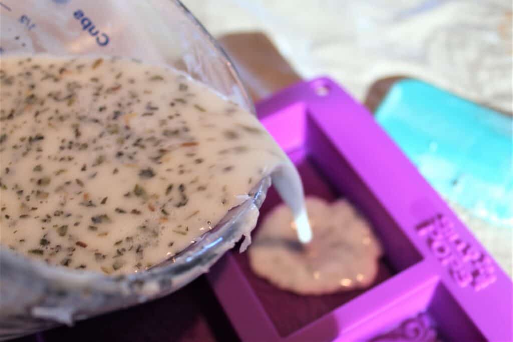 pouring goat milk liquid soap with peppermint leaves into soap molds