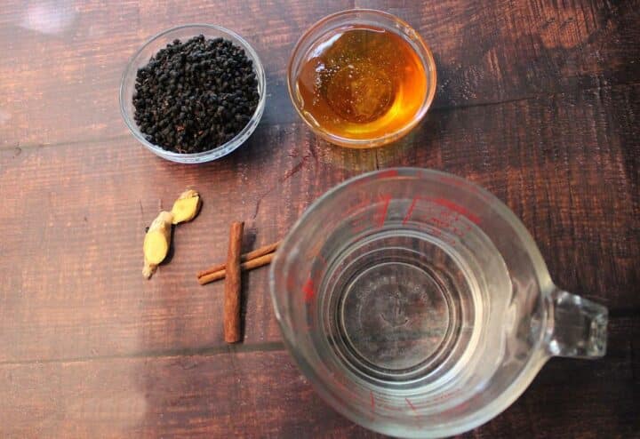 A bowl of black tea, cinnamon sticks, and other ingredients on a wooden table.