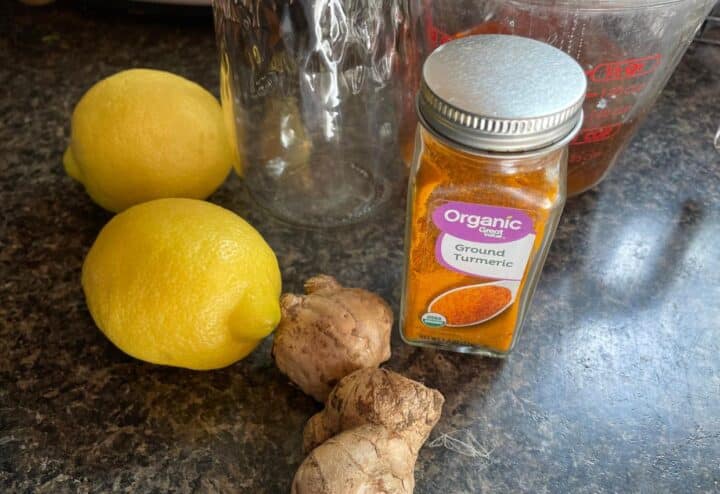 A jar of turmeric, lemons and ginger on a counter.