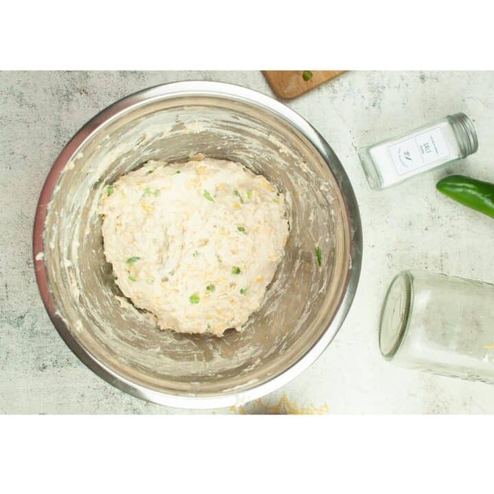 A bowl of dough with cheese and peppers next to it.