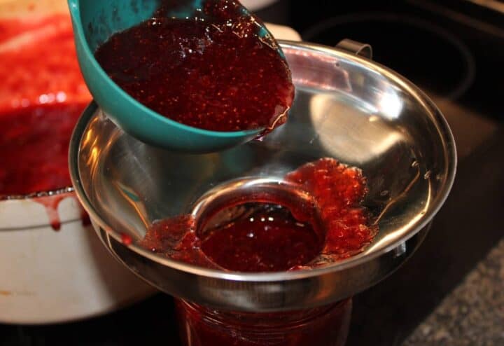 Ladling prepared strawberry jam into clean mason jars.