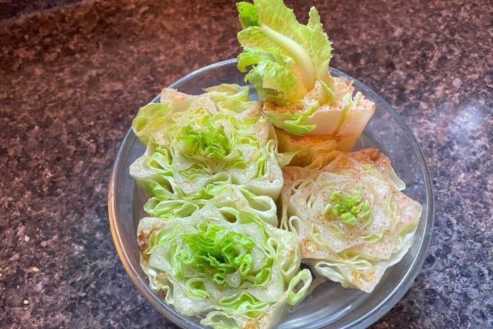 A bowl of fresh lettuce wraps filled with seasoned minced meat on a kitchen countertop.