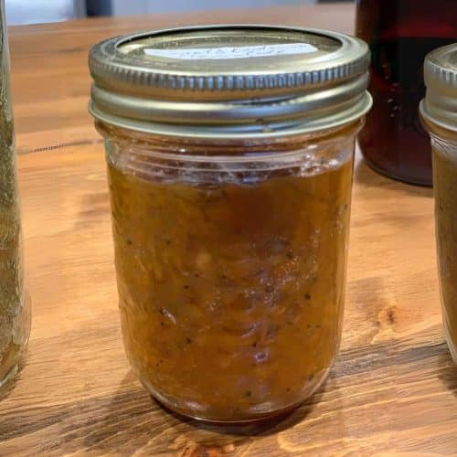 Three jars of homemade preserves on a wooden table, with one showing chunky orange marmalade and others appearing less textured.