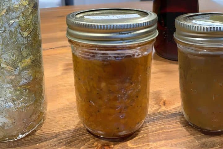Three jars of homemade preserves on a wooden table, with one showing chunky orange marmalade and others appearing less textured.