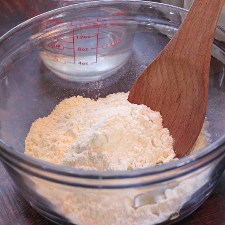 Flour in glass mixing bowl with wooden spoon.