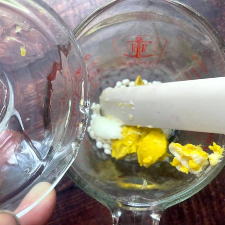 A person is mixing beeswax pellets, shea butter and coconut oil in a glass bowl.