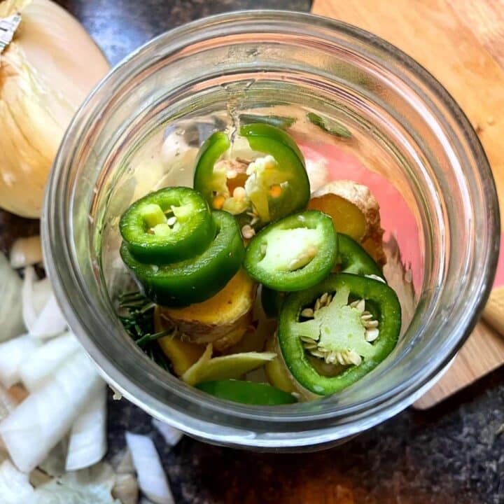 Jalapenos and onions in a jar on a cutting board.