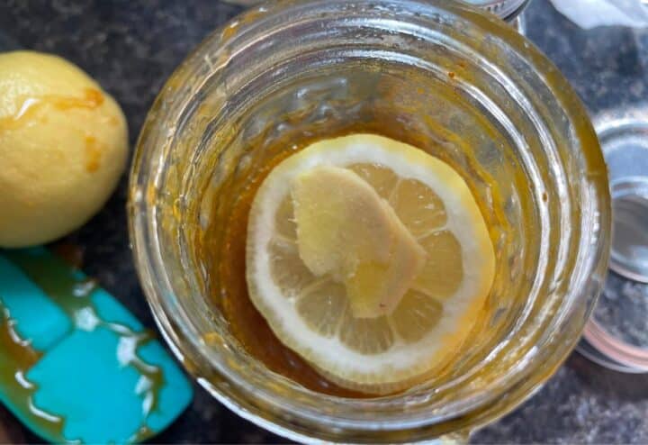 A jar of lemon juice with a slice of lemon next to it.