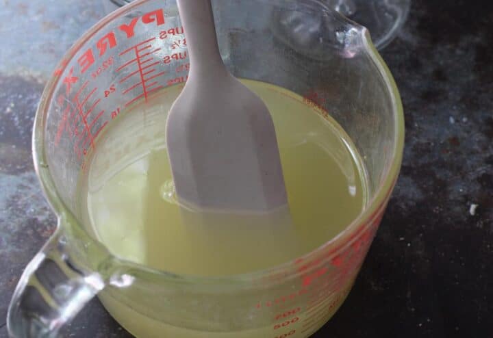 A measuring cup with a spoon in candle mixture.