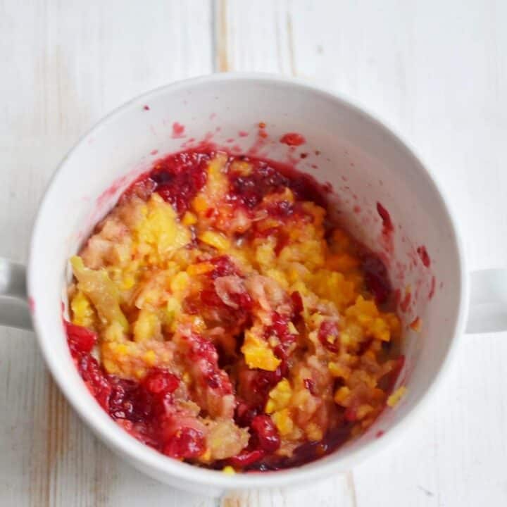 Cranberries, apples, oranges in a bowl on a wooden table.