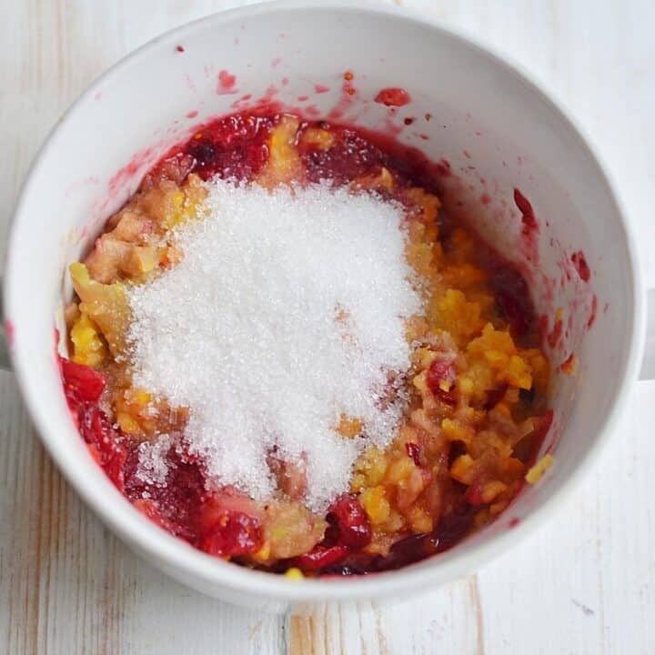 Sugar, apples, oranges, and cranberries in a bowl.