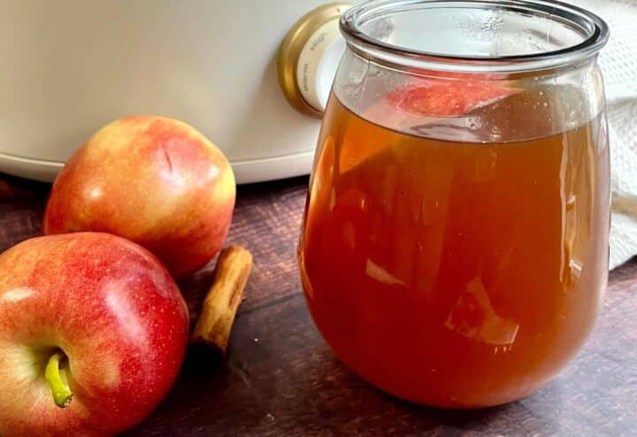 A jar of apple juice next to apples.