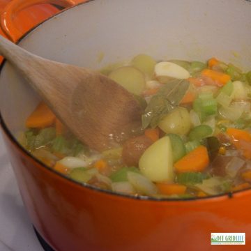 a orange dutch oven pot with celery, carrots and potatoes simmering